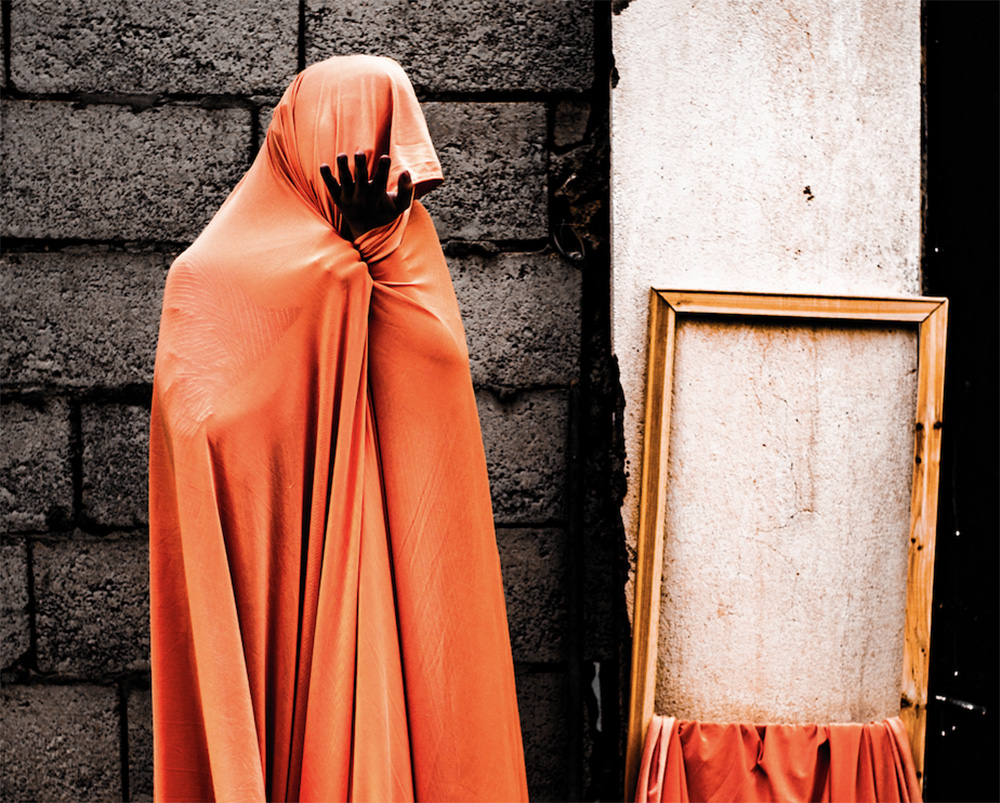 A red hooded figure stands next to an empty picture frame