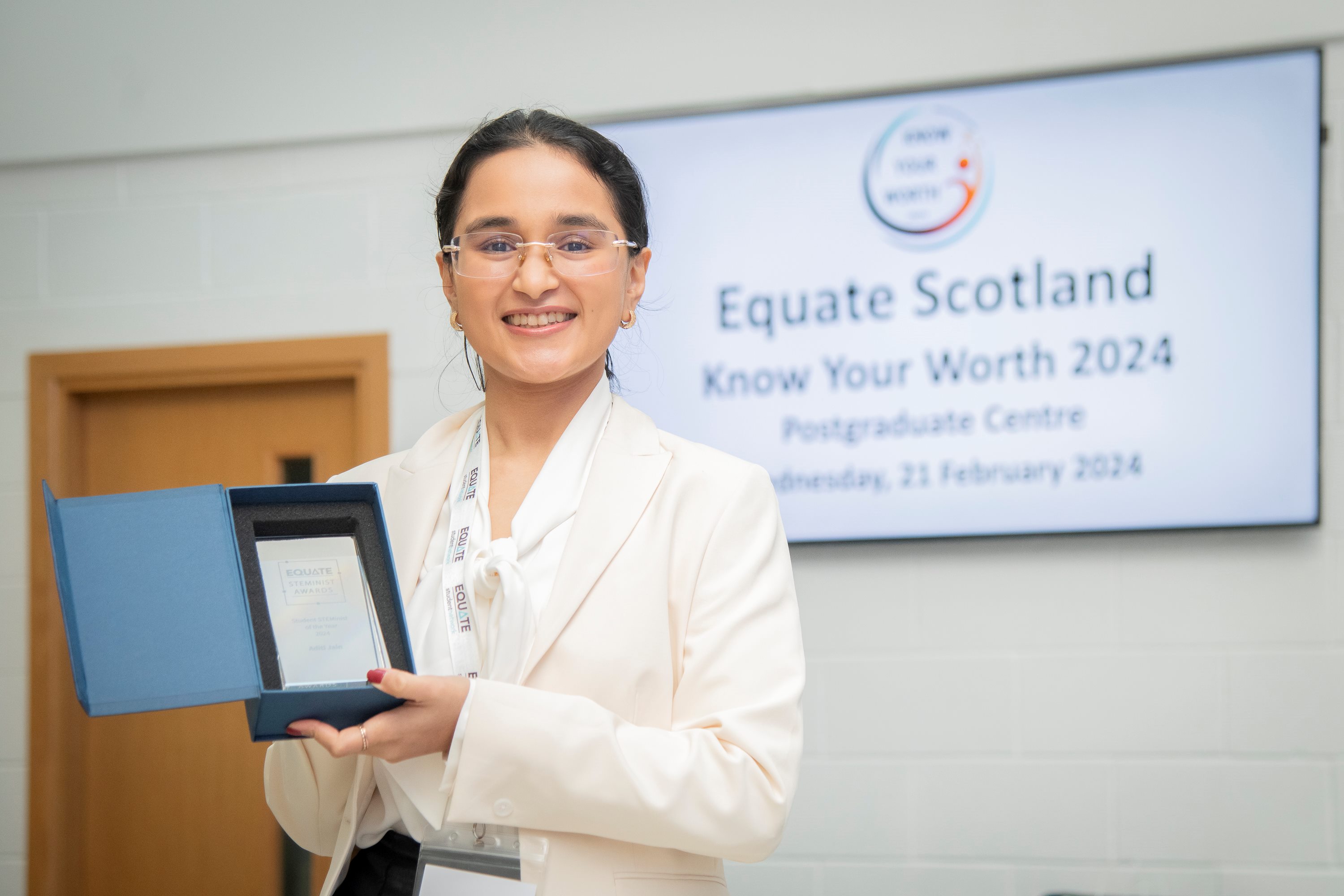 Portrait of Aditi Jain standing in front of a screen with the writing 'Equate Scotland'