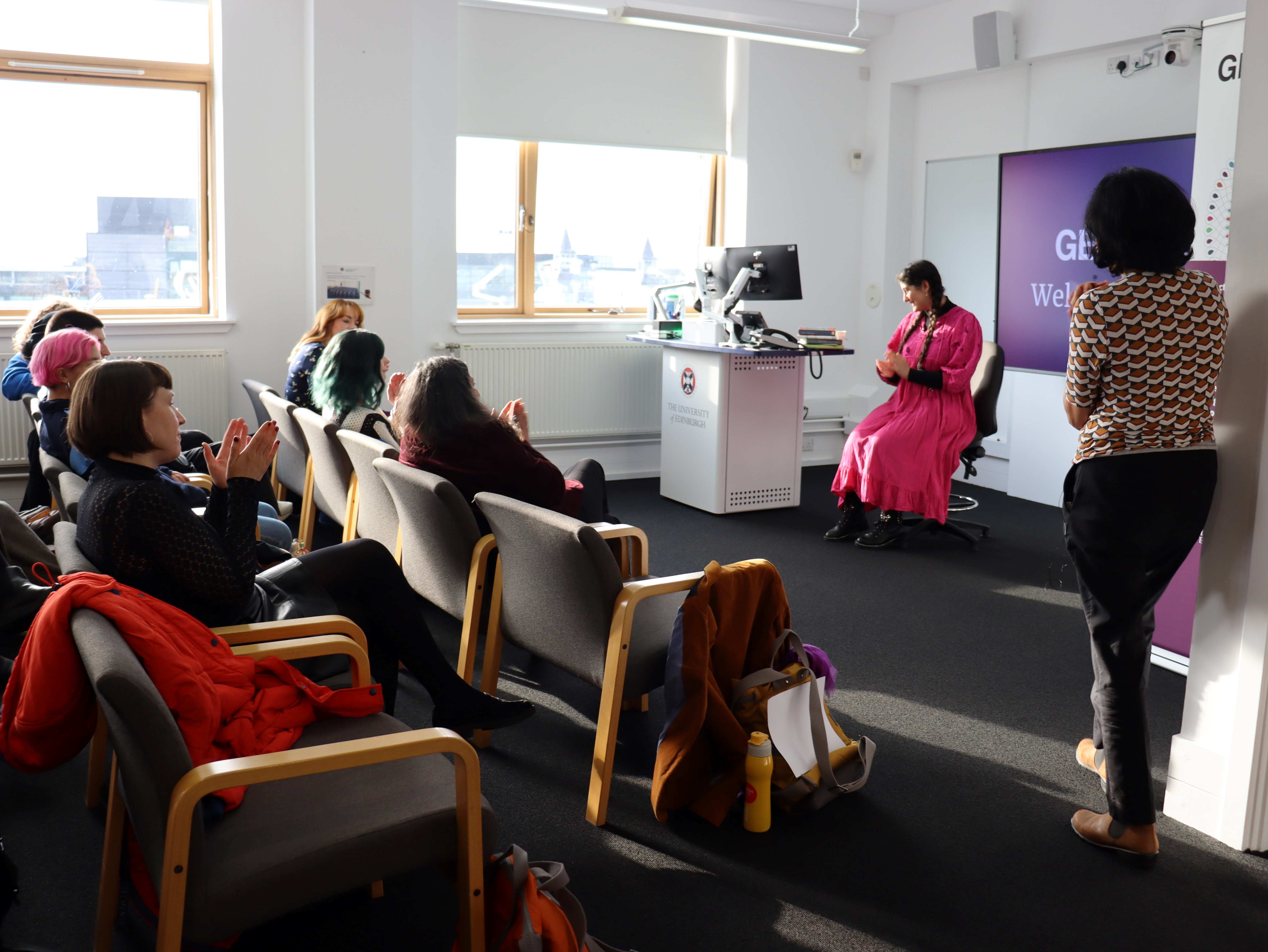Picture of GENDER.ED's welcome reception where the feminist trailblazer awards were awarded. It shows poet Nadine Aisha Jassat sitting on a chair after reading out her poetry in front of two rows of people sat on chairs.