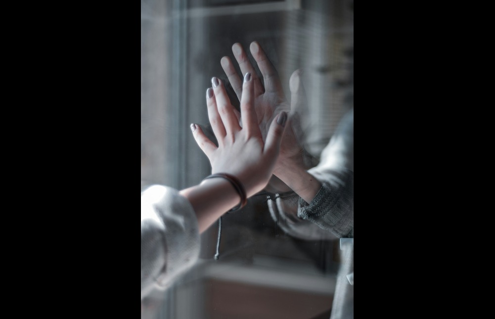 A woman's arm with a silver and red bracelet, poised against a mirror