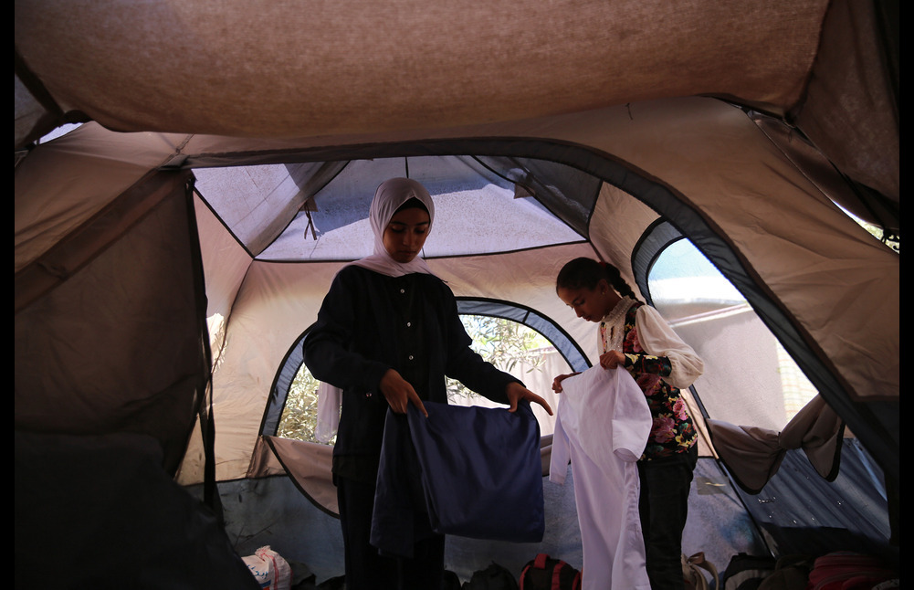 Two girls in Gaza fold clothes inside their family’s tent.