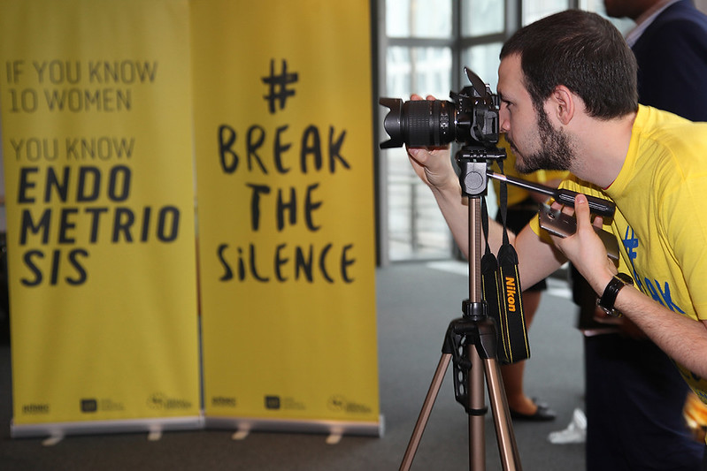 Person in a yellow t shirt photographing an Endometriosis Awareness board