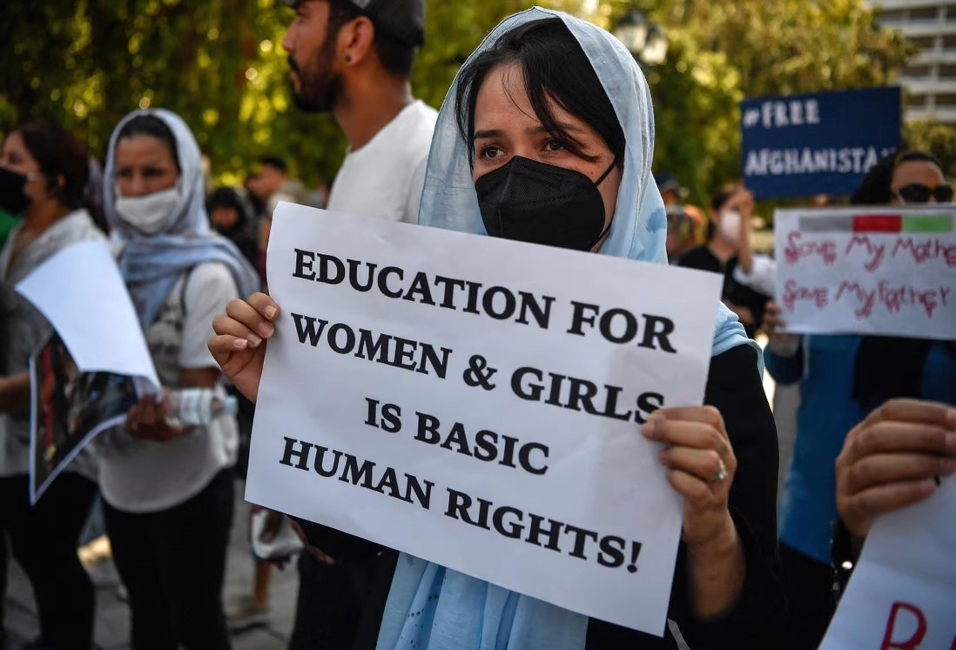 woman at a protest, holding a sign saying 'education for women and girls is basic human rights!'