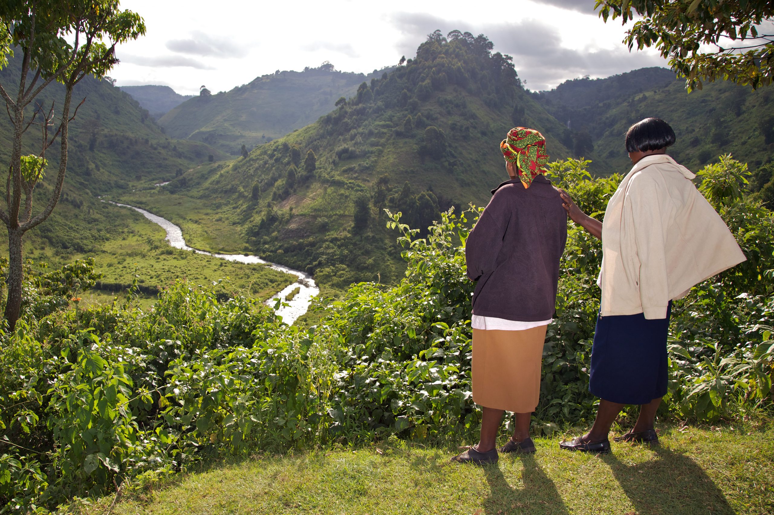 Two women looking out over a natural area with hills, grass and a stream.