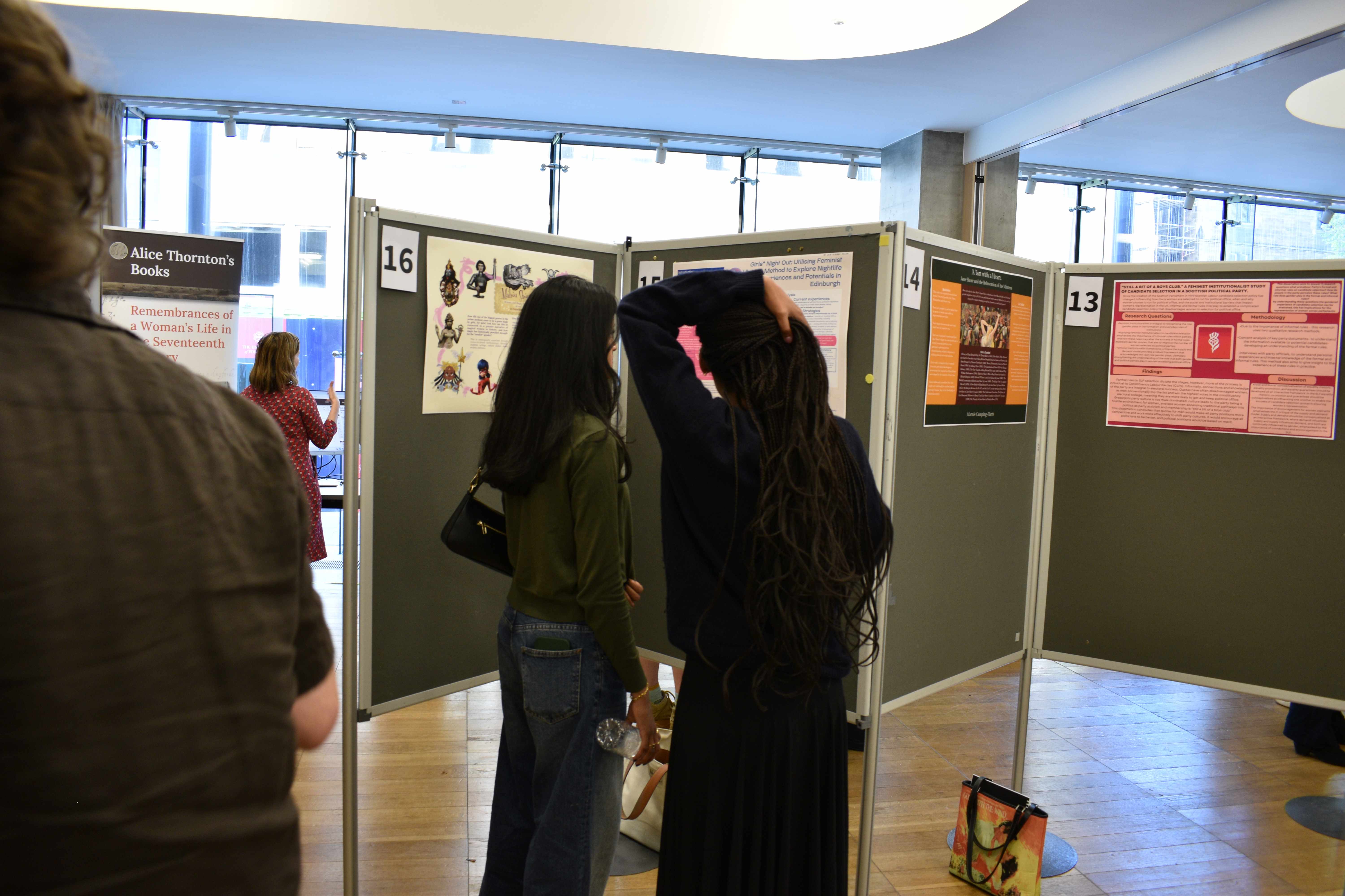 Photo of two undergraduate students looking at a poster by another undergraduat student at the Mini Undergraduate Dissertation Showcase.