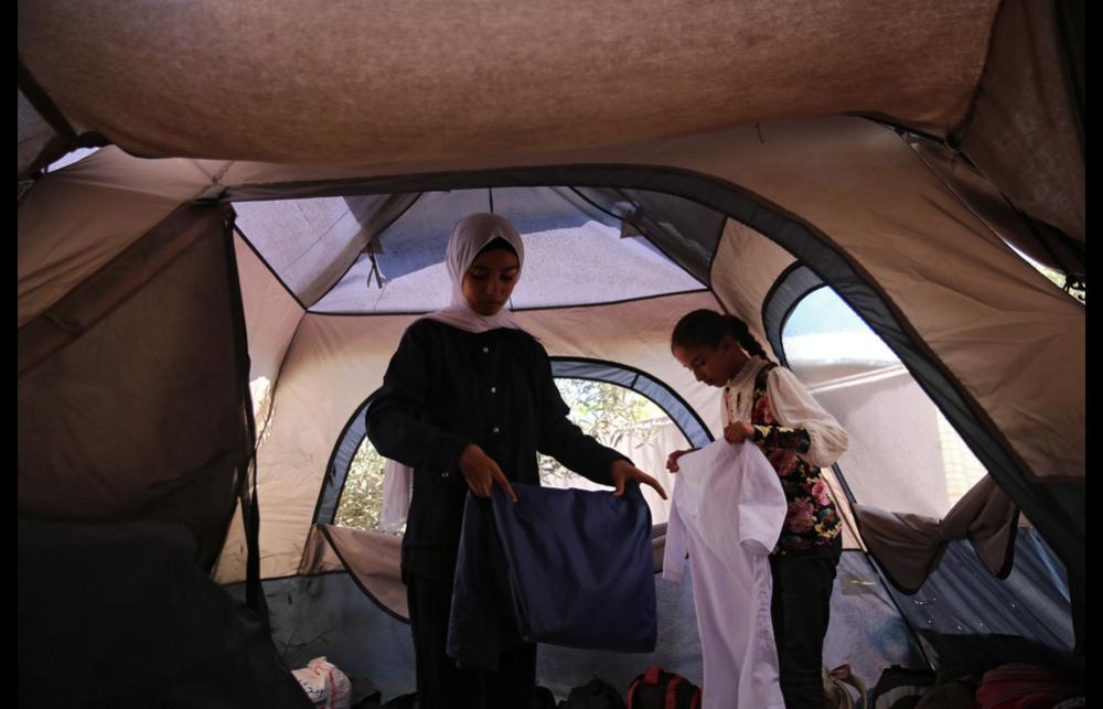 Two girls in Gaza fold clothes inside their family’s tent. 