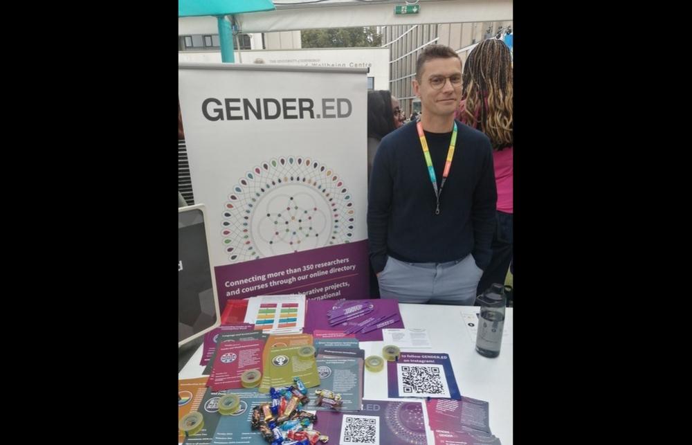 Photo of Wannes Dupont next to a GENDER.ED poster and in front of a table laden with flyers and sweets